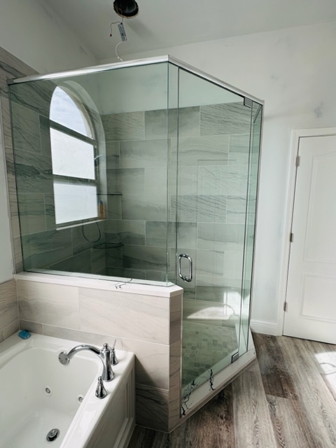 A Glass Panel Shower Beside a Ceramic Tub With Fittings